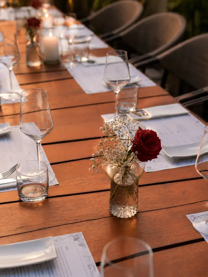 Lange gedeckte Tafel mit Kerzen und Rosen im Innenhof in der Abenddämmerung