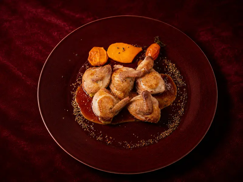 Gebratenes Geflügel mit Jus und Karotte, angerichtet auf dunklem Teller